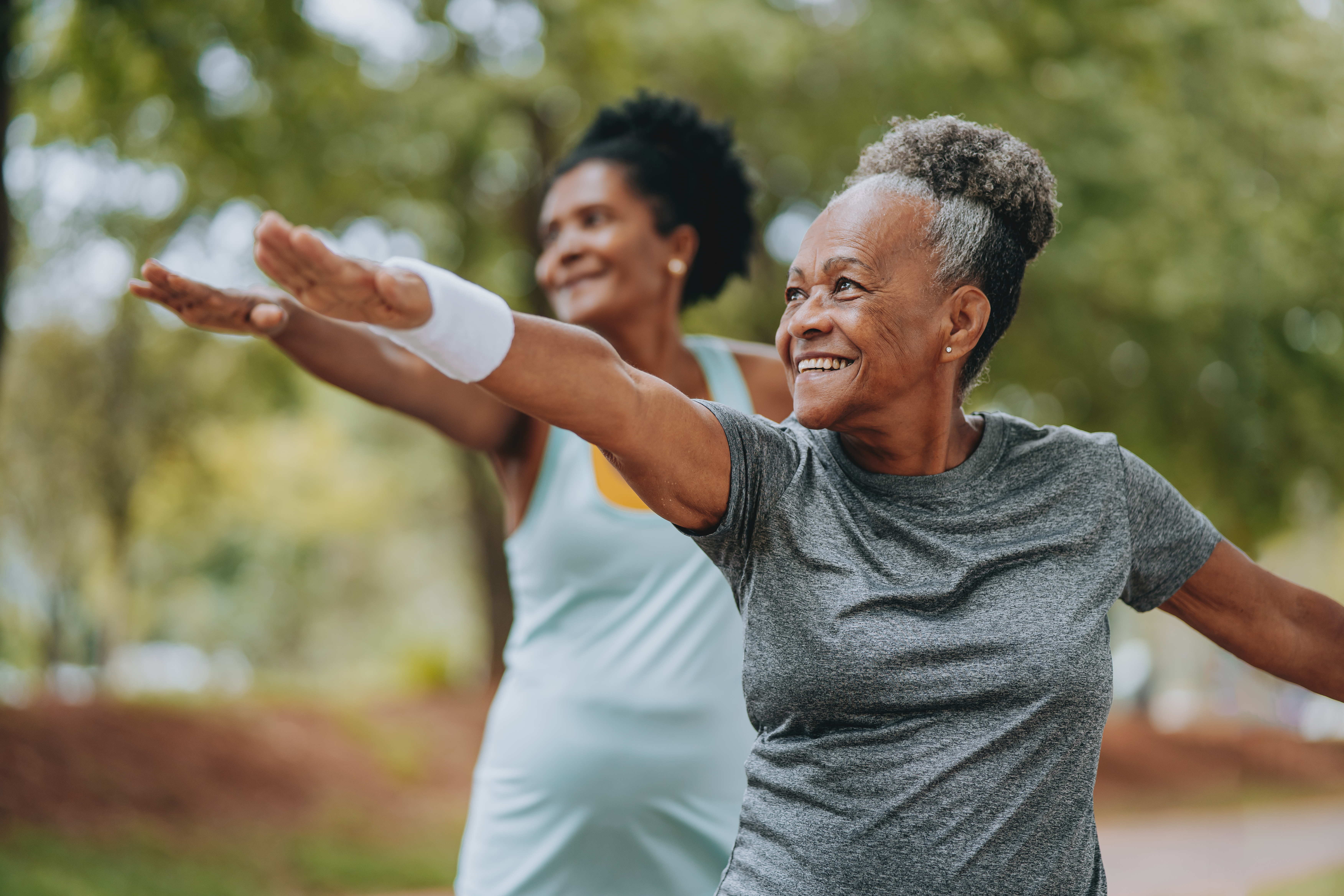 Two women enjoying outdoor yoga, smiling with arms outstretched.