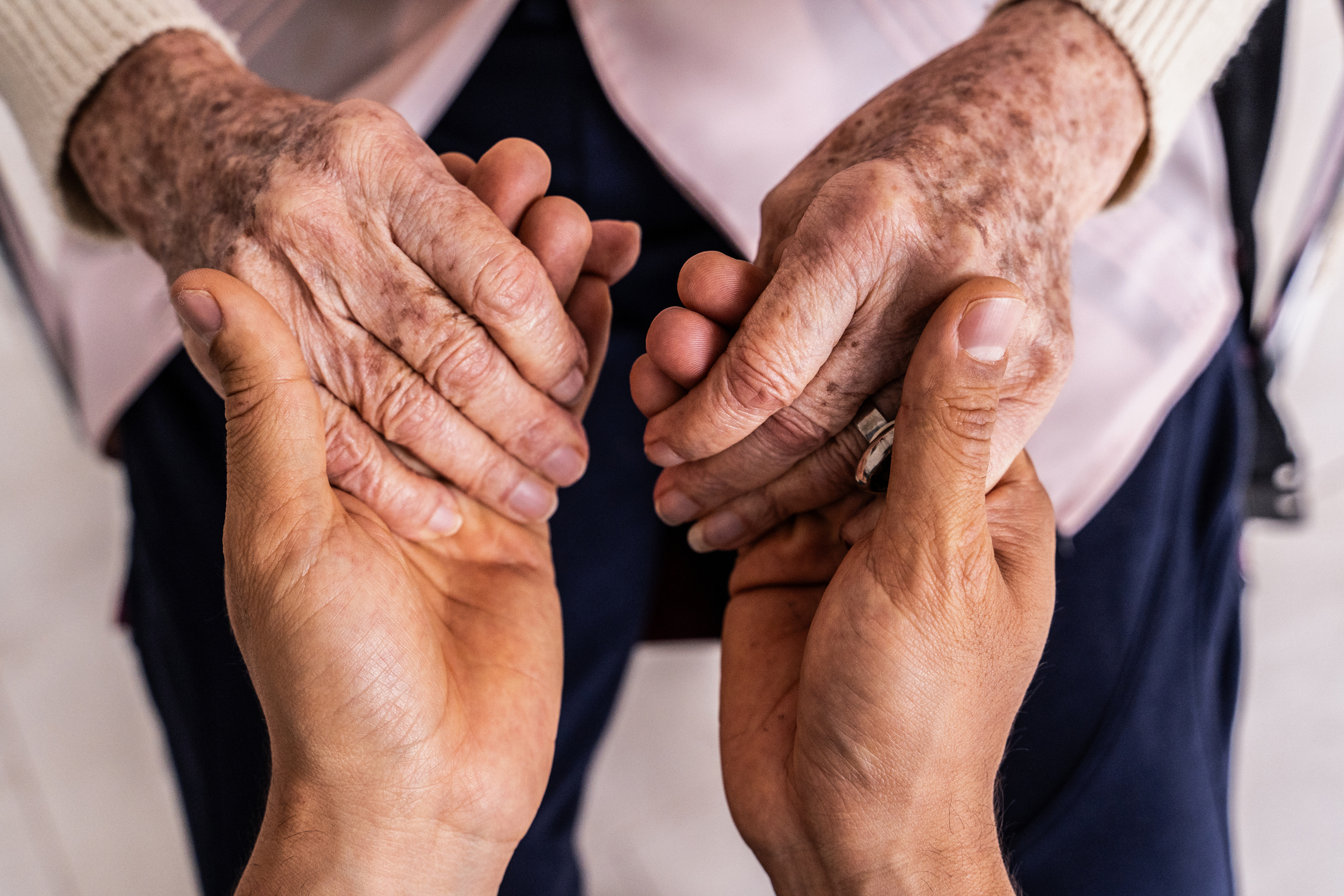 Elderly hands held gently by younger hands, conveying care.