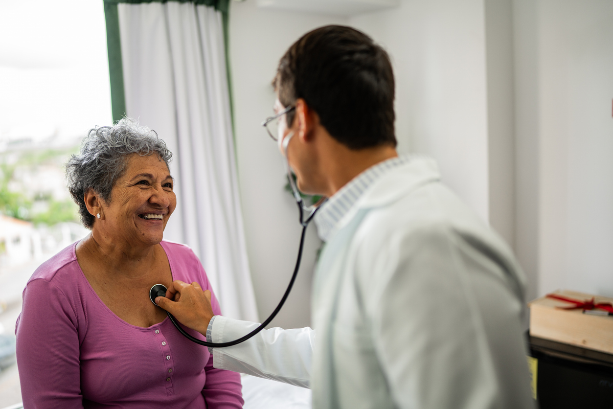 An elderly woman having her chest listened to by her doctor