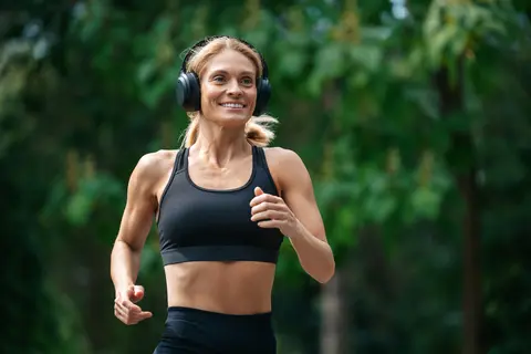 Woman jogging in a park, wearing headphones and a black sports bra.