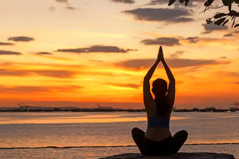 Person doing yoga at sunset by the ocean.