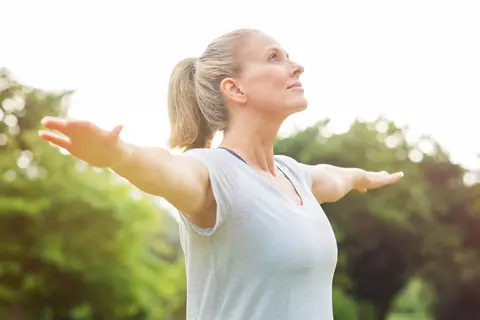 Woman stretching arms outside, looking upward, in a green park.