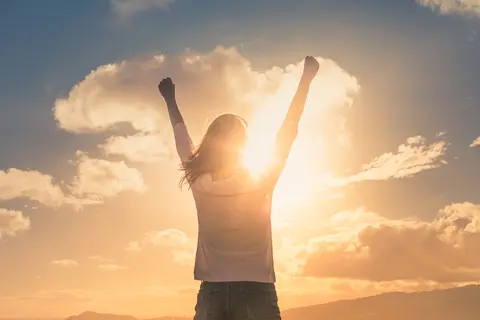 Person celebrates with raised arms at sunset.