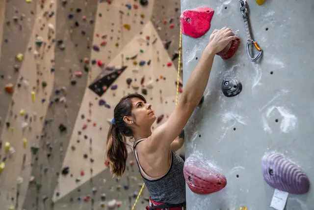 Woman climbing an indoor rock wall with colorful holds.