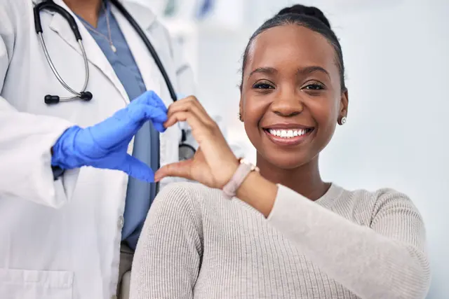 Doctor and smiling patient form a heart with hands.