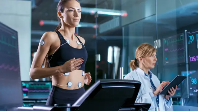 Woman on treadmill with sensors, doctor monitoring data on tablet.