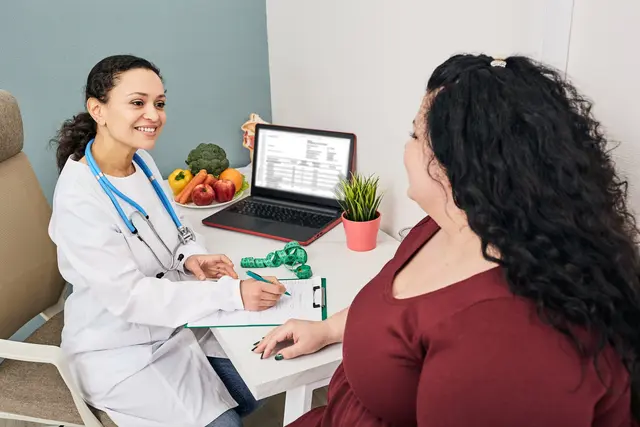 Doctor chatting with a patient, fruits and a laptop on the desk.