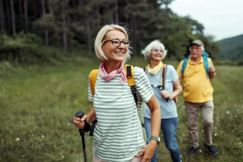 Elderly hikers smiling and walking through a grassy field.