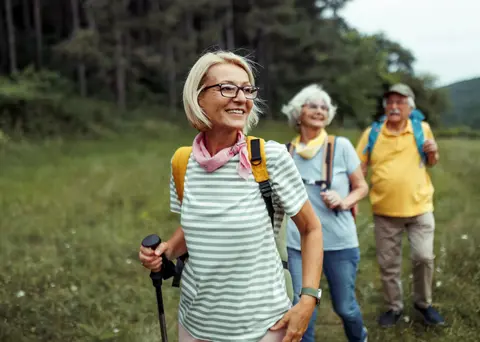 Elderly hikers smiling and walking through a grassy field.