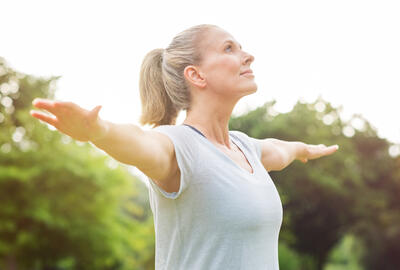 Woman stretching arms outside, looking upward, in a green park.