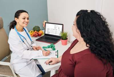 Doctor chatting with a patient, fruits and a laptop on the desk.