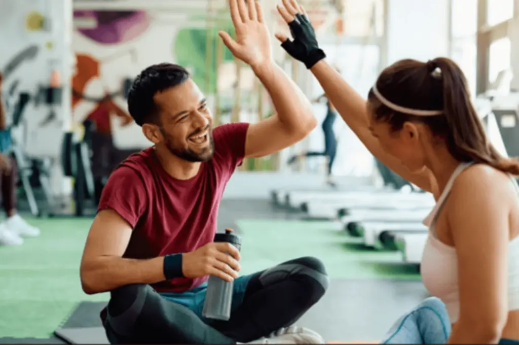 A man and woman high-five on a gym floor, smiling brightly.