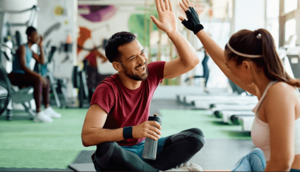 A man and woman high-five on a gym floor, smiling brightly.