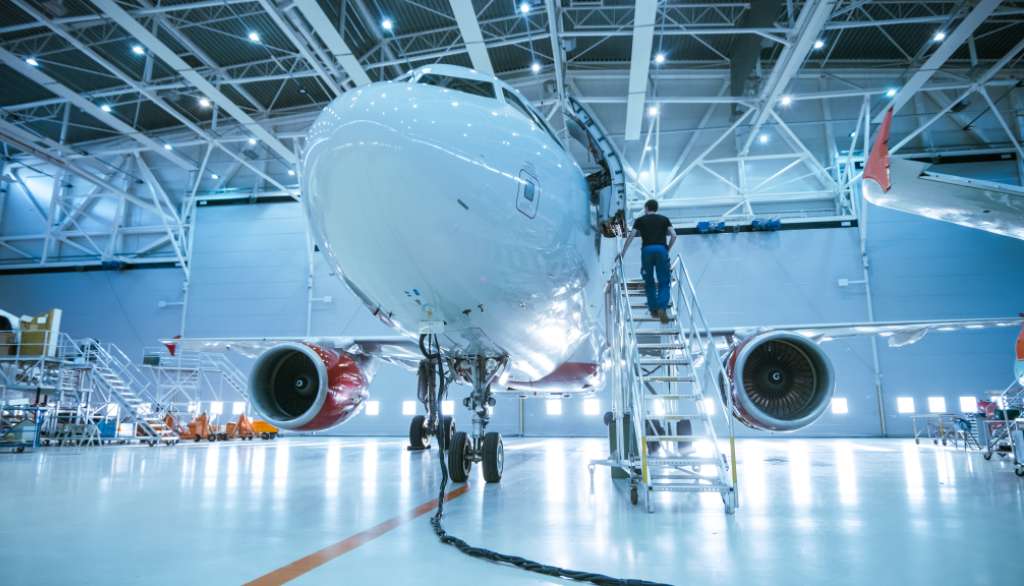 Aircraft in hangar with technician on a ladder.