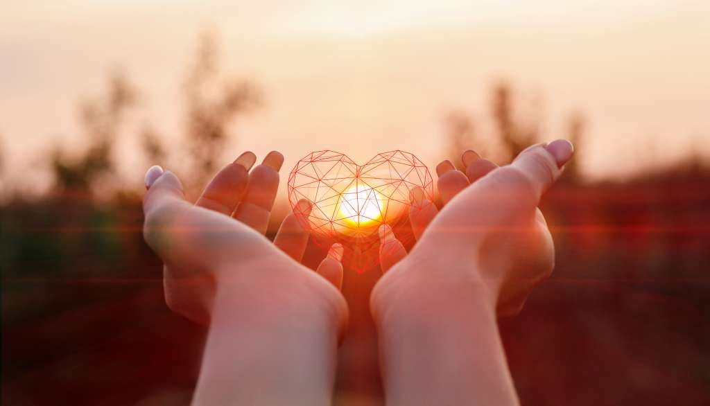Hands holding a 3d heart illuminated by a setting sun