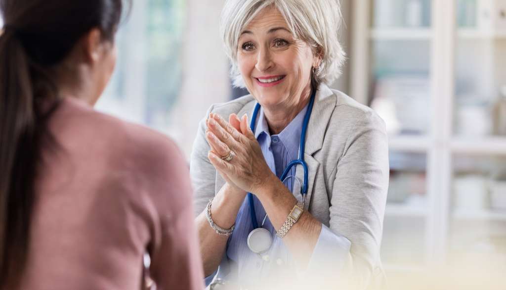 Doctor with stethoscope smiling and talking to a patient.