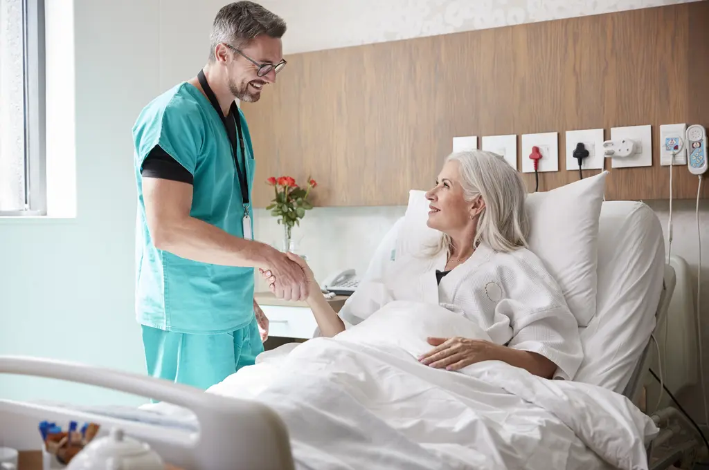 Doctor shaking hands with smiling patient in hospital bed.