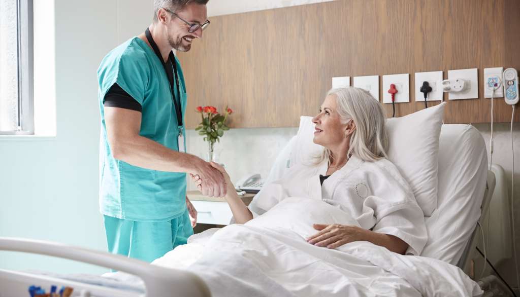 Doctor shaking hands with smiling patient in hospital bed.