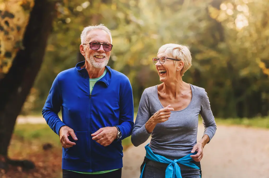 Smiling elderly couple jogging in a sunny park.