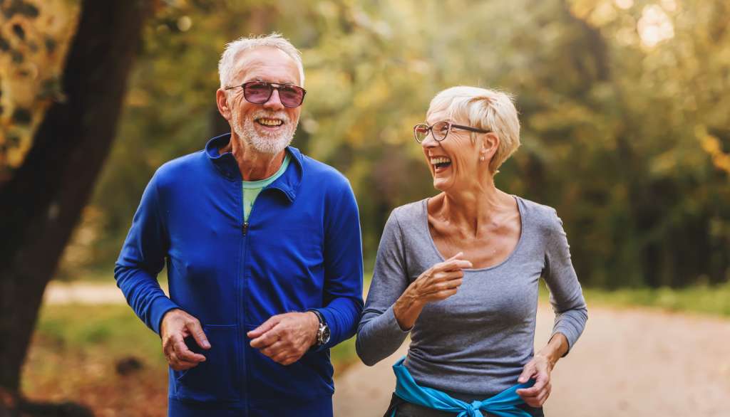 Smiling elderly couple jogging in a sunny park.