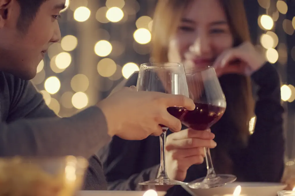 Toasting red wine glasses in a romantic, softly-lit setting.