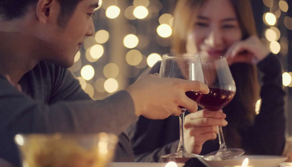 Toasting red wine glasses in a romantic, softly-lit setting.