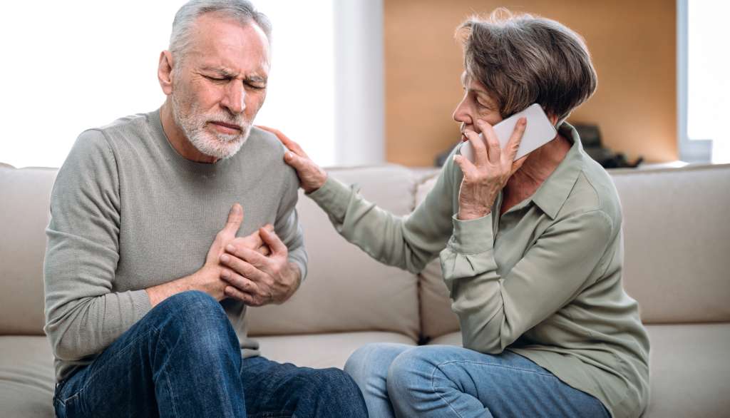 Man clutching chest, woman on phone, looking concerned.