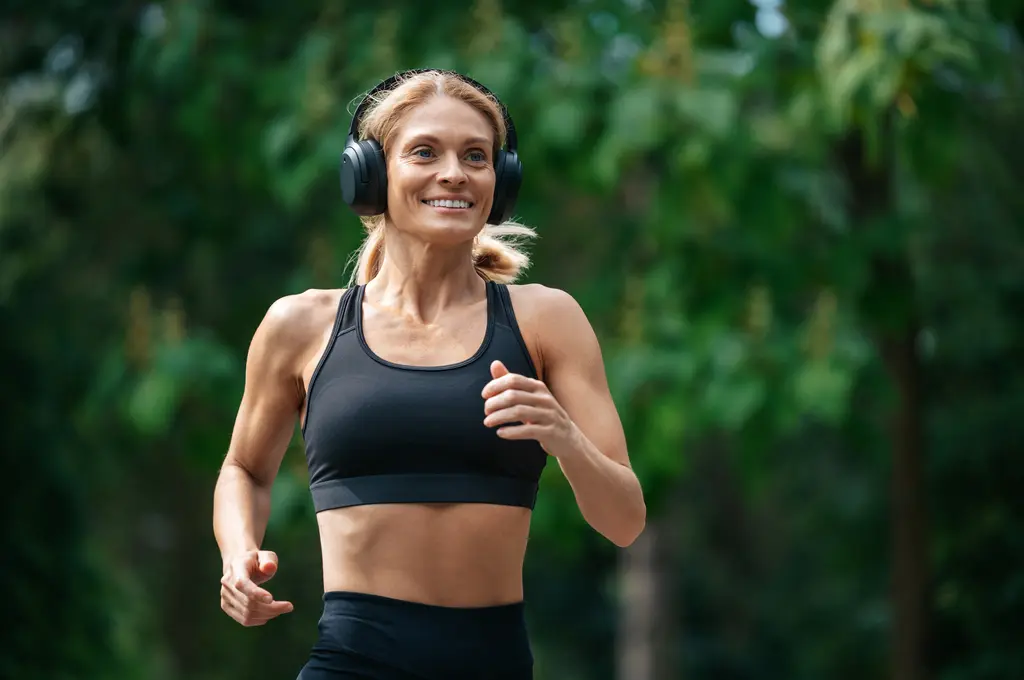 Woman jogging in a park, wearing headphones and a black sports bra.