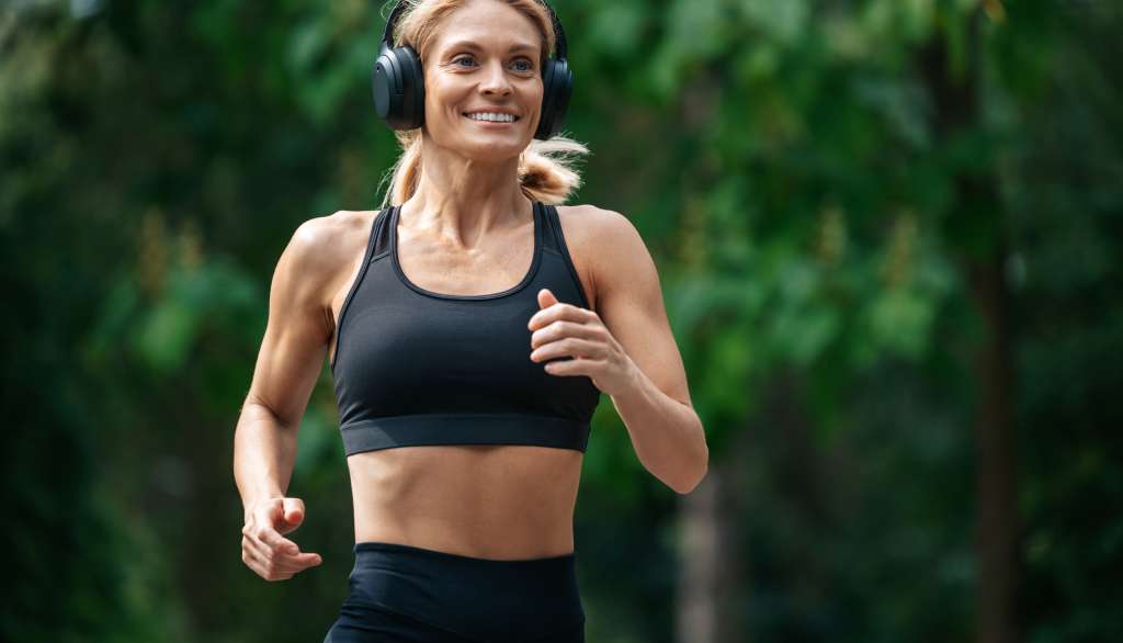 Woman jogging in a park, wearing headphones and a black sports bra.
