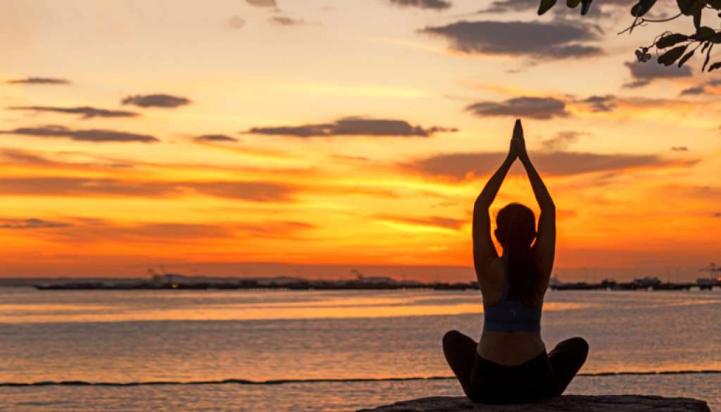 Person doing yoga at sunset by the ocean.