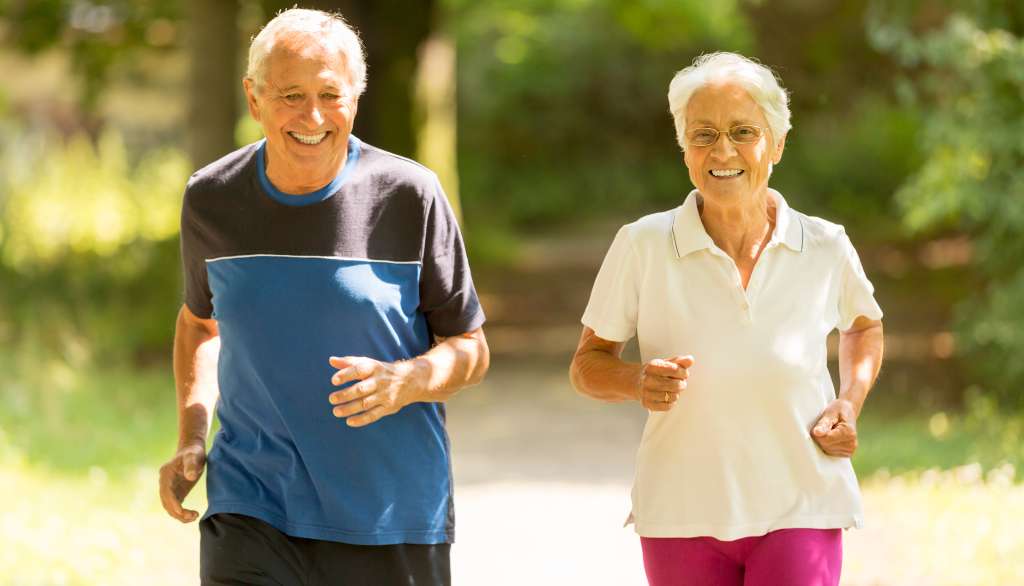 Elderly couple jogging outdoors, smiling brightly.