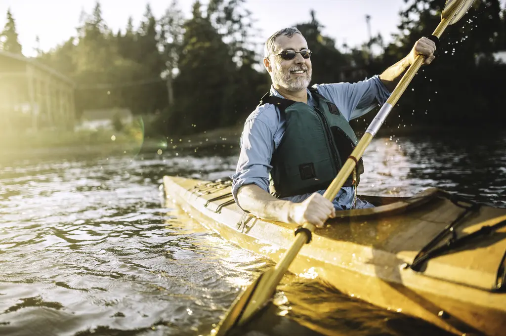 Man kayaking on a sunlit lake, smiling, wearing sunglasses and a life jacket.