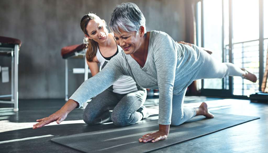 Woman doing yoga balance pose with trainer's guidance.