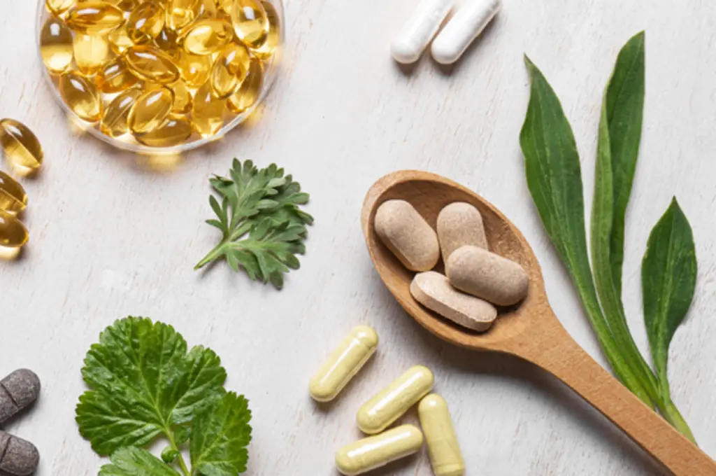 Herbal supplements and capsules on a light surface with green leaves.