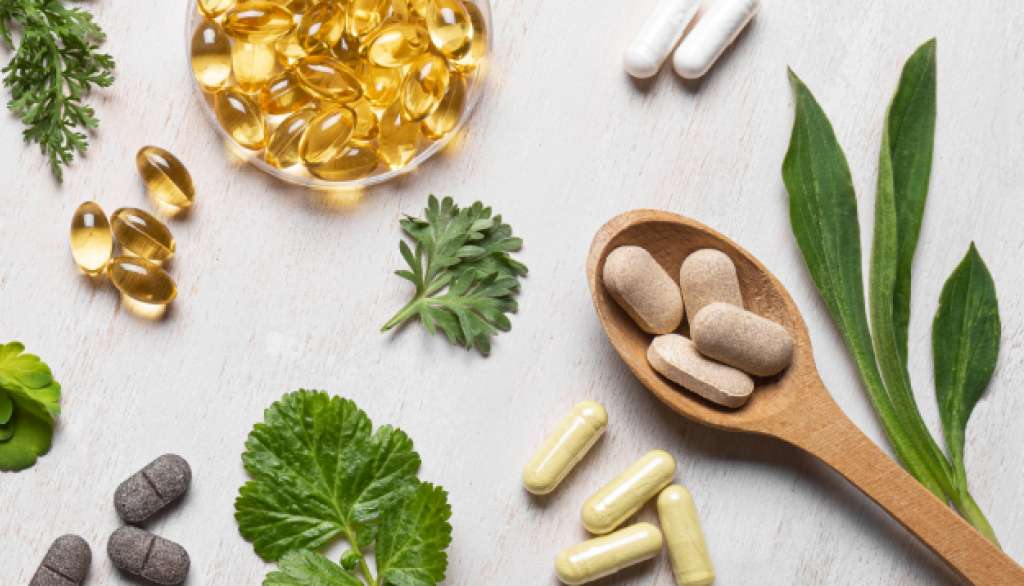 Herbal supplements and capsules on a light surface with green leaves.