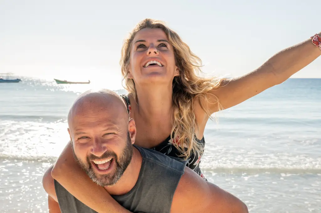 Smiling couple piggybacking on a sunny beach day.