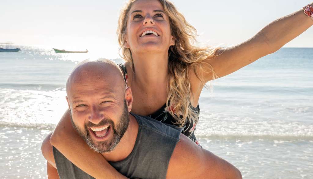 Smiling couple piggybacking on a sunny beach day.