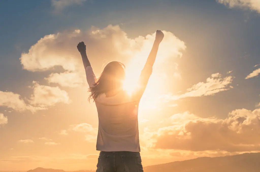 Person celebrates with raised arms at sunset.