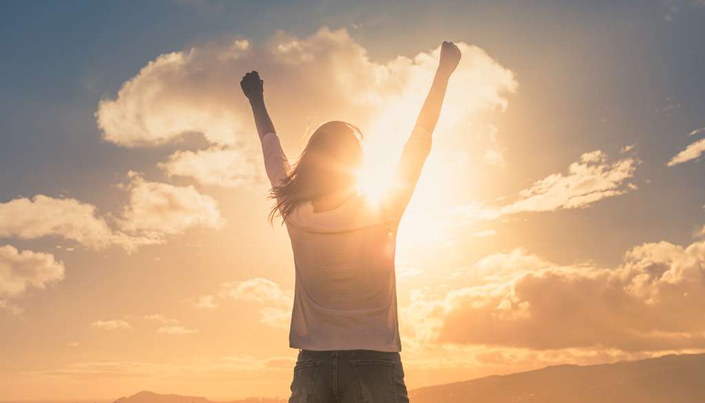 Person celebrates with raised arms at sunset.