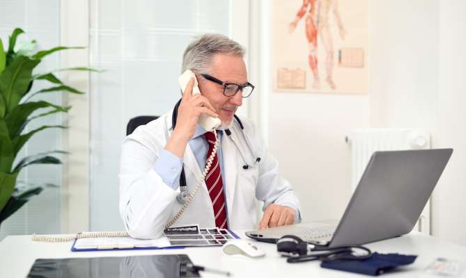 Male doctor talking on phone at desk with laptop open