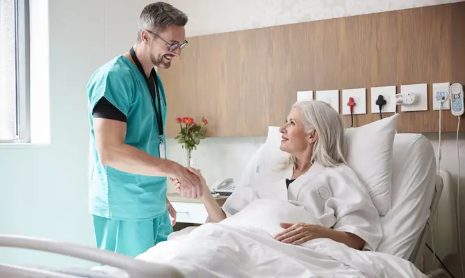 Doctor shaking hands with smiling patient in hospital bed.