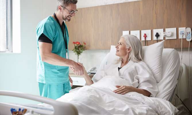 Doctor shaking hands with smiling patient in hospital bed.