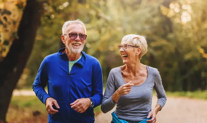 Smiling elderly couple jogging in a sunny park.