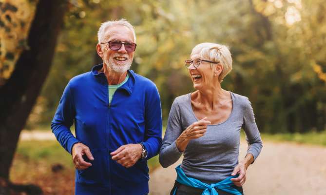 Smiling elderly couple jogging in a sunny park.