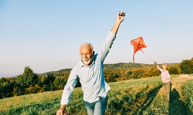Happy middle-aged couple running and flying a red kite in an open field