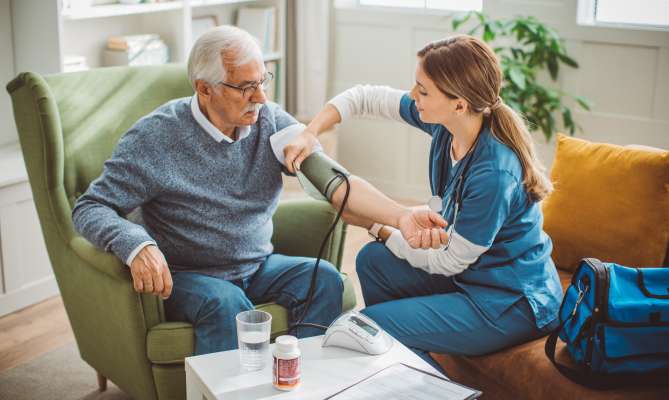 Nurse checking an elderly man's blood pressure at home.