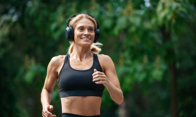 Woman jogging in a park, wearing headphones and a black sports bra.