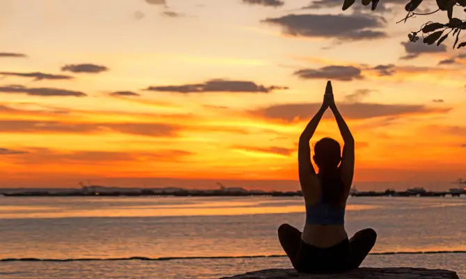 Person doing yoga at sunset by the ocean.