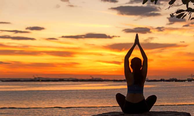Person doing yoga at sunset by the ocean.
