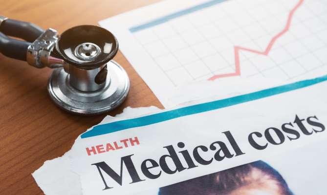 Stethoscope on table with rising medical costs graph.